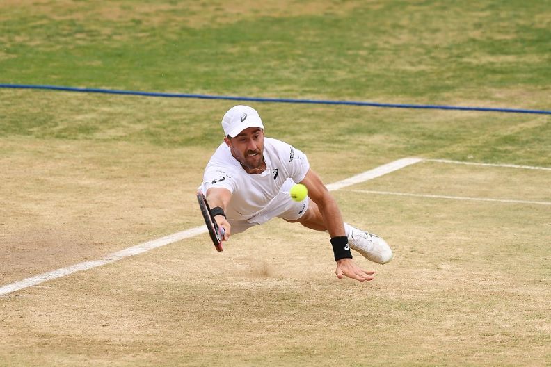 male tennis player dives for the ball with his racquet extended outward