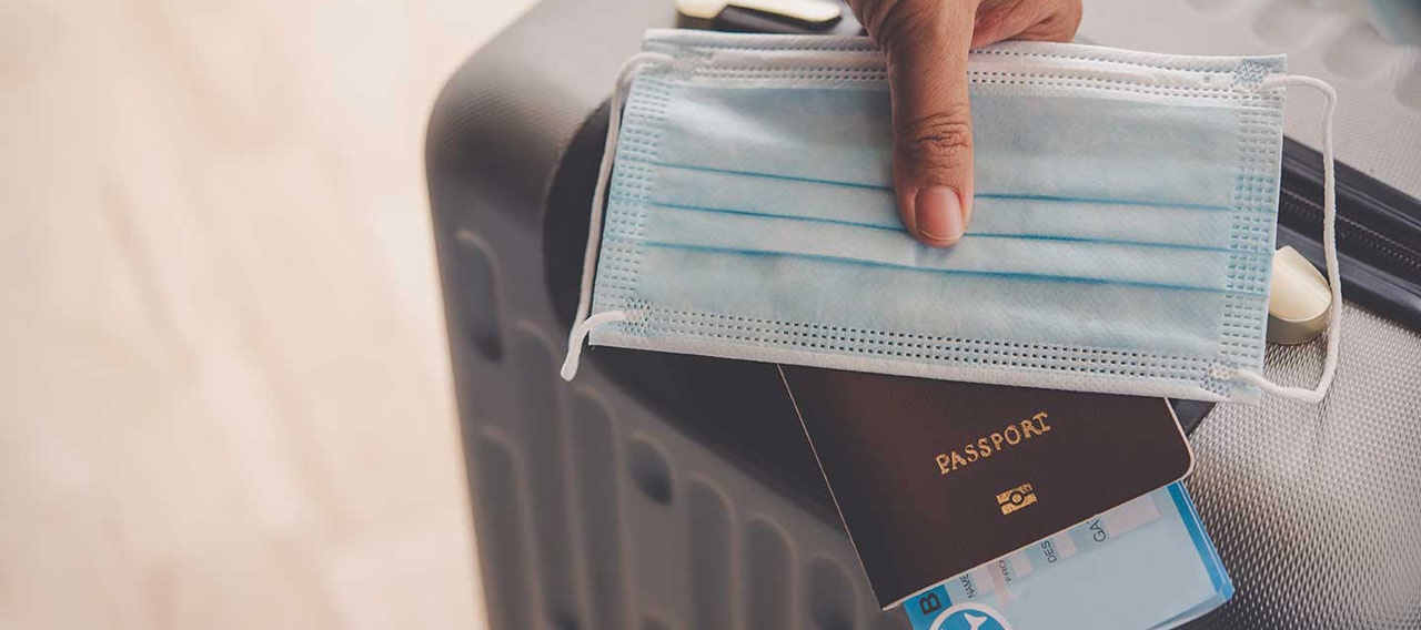 hand with mask, passport, and suitcase